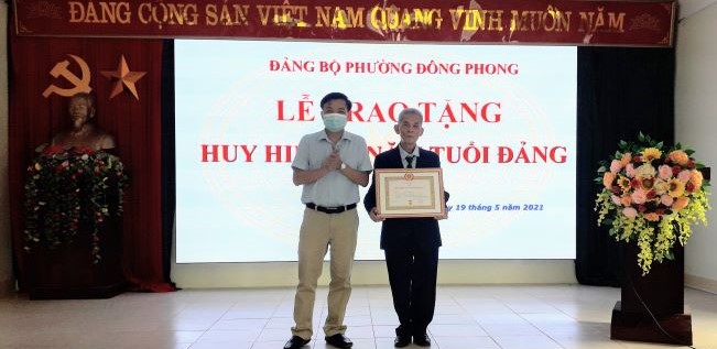 Đồng chí Đàm Vũ Hùng – ThUV, Bí thư Đảng ủy phường Đông Phong trao huy hiệu 50 năm tuổi Đảng cho đảng viên Giang Văn Thế.